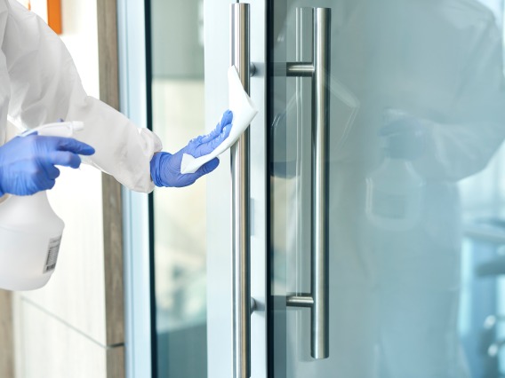 A stock image of a person disinfecting a door 